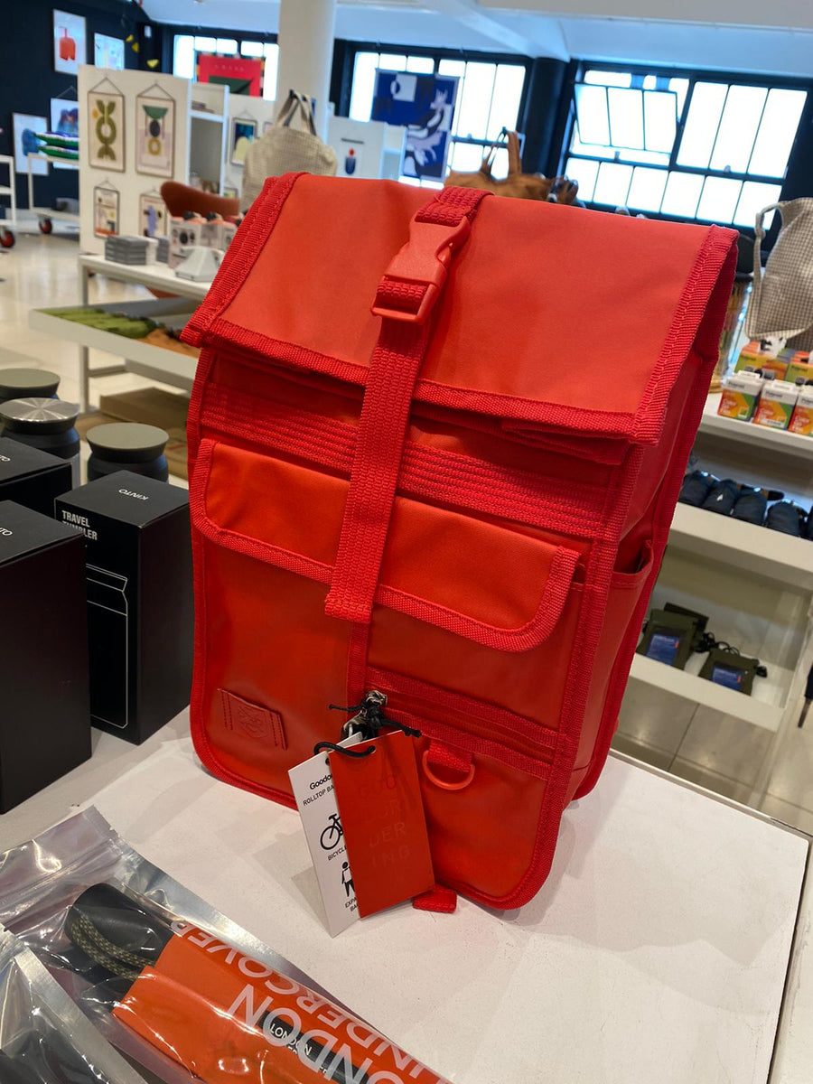 Red rolltop  backpack with a flap top and front pockets, Displayed in the conran shop