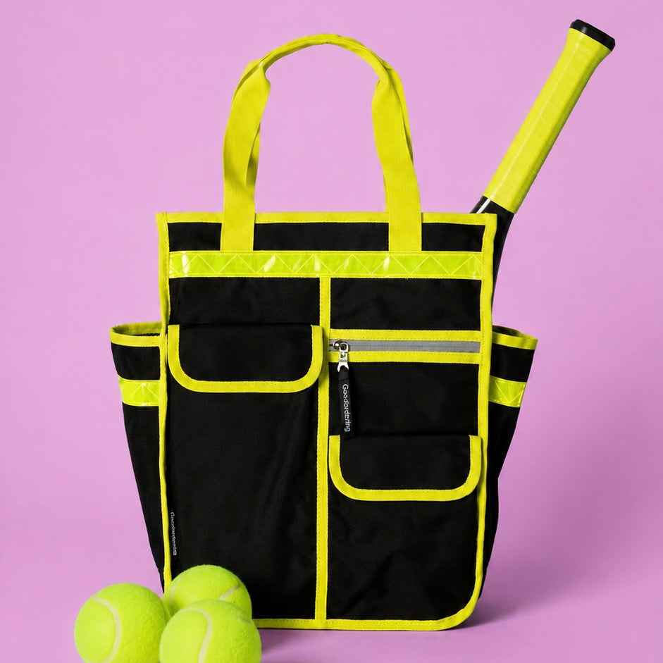 A black and neon yellow tennis tote bag with a tennis racket tucked into the side pocket and three tennis balls in the foreground, set against a solid lavender background.